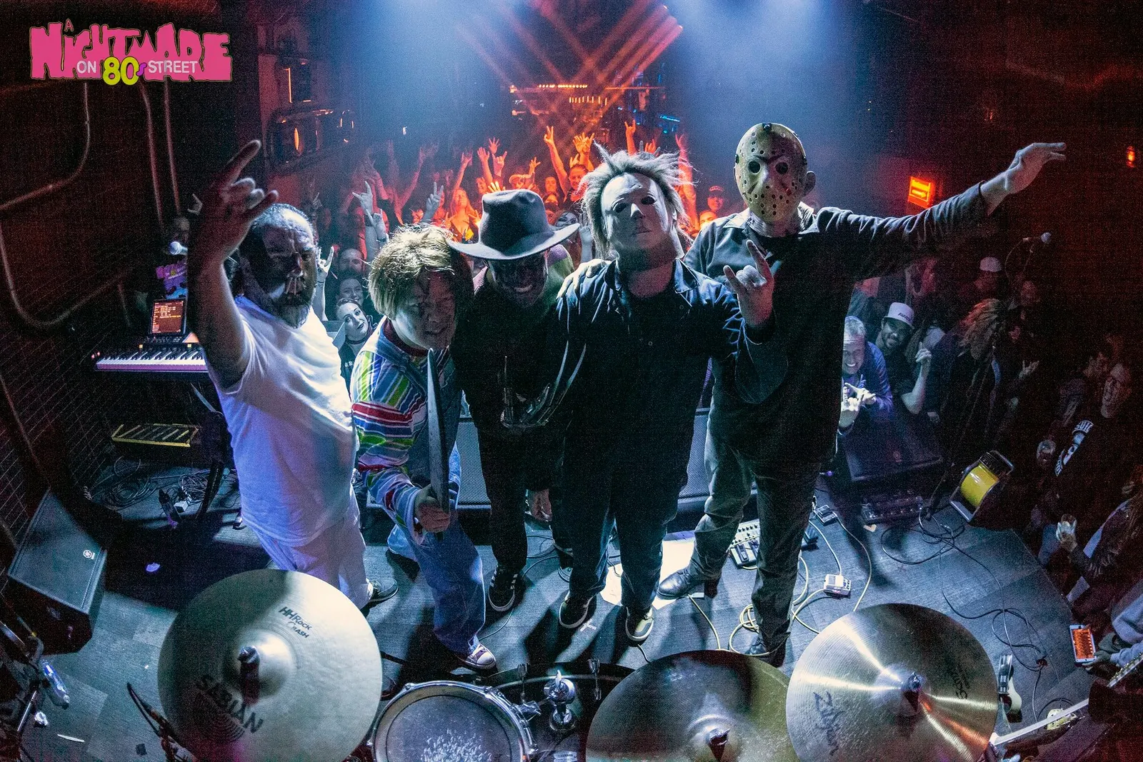 The full band in horror costumes posing onstage with the crowd behind them